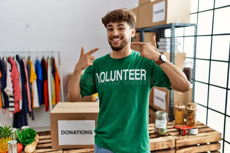 young-arab-man-wearing-volunteer-t-shirt-donations-stand-smiling-cheerful-showing-pointing-fingers-teeth-mouth-dental-253693932